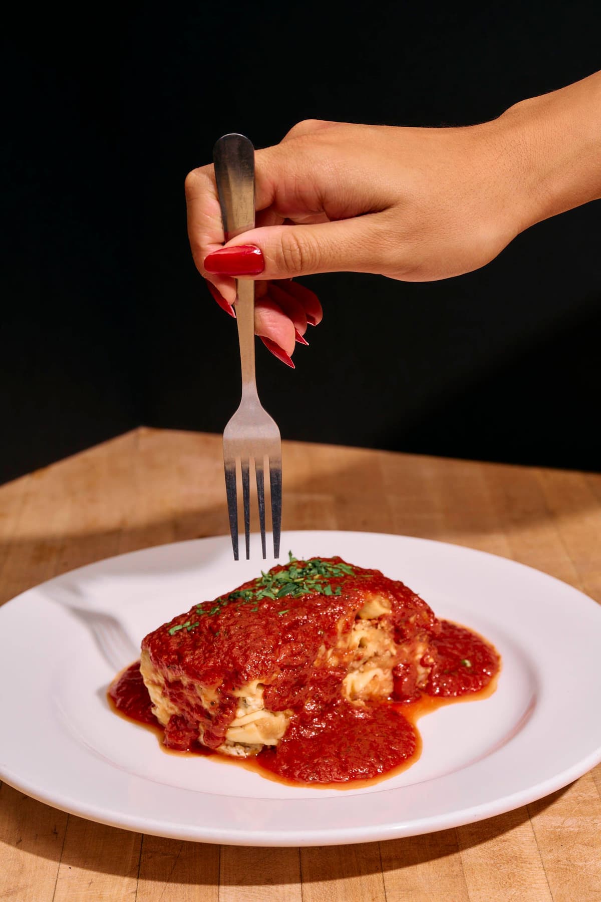 A hand with fork about to cut into a piece of lasagna.